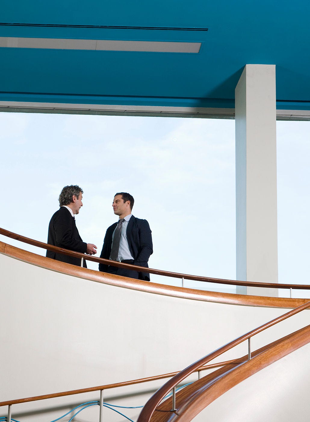 Two businessman hold a conversation on a balcony.