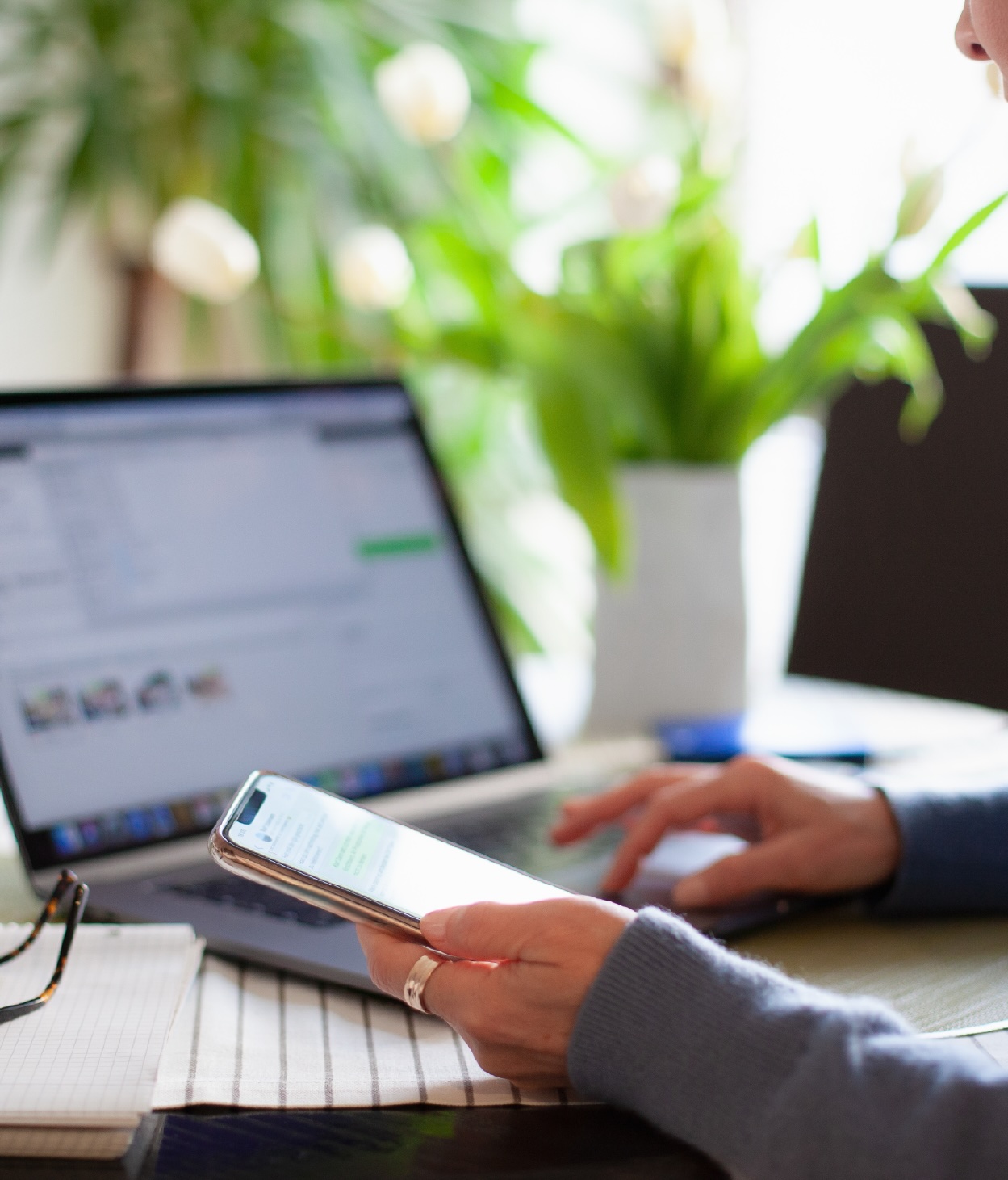 Person using a mobile phone while typing on a laptop.
